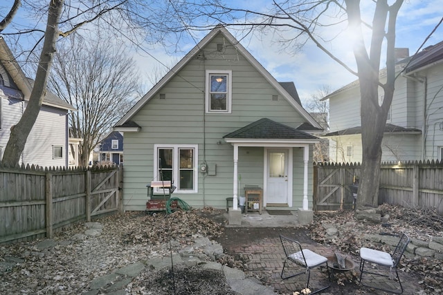 rear view of property featuring a shingled roof, a fenced backyard, and a gate