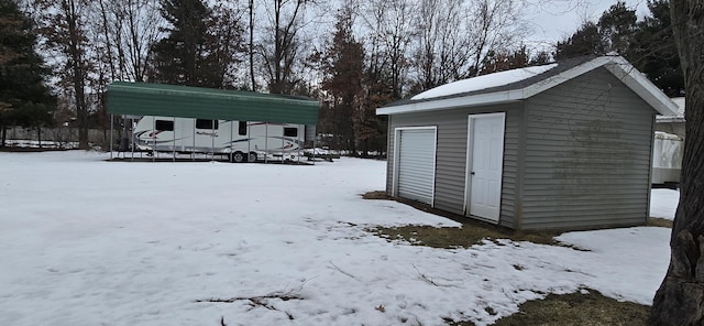 snow covered structure featuring an outbuilding and a detached carport