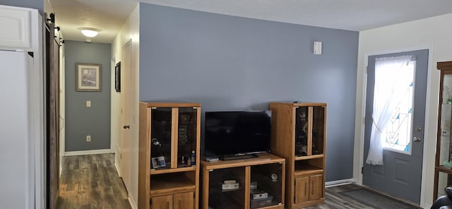 living area with a barn door, dark wood-style flooring, and baseboards