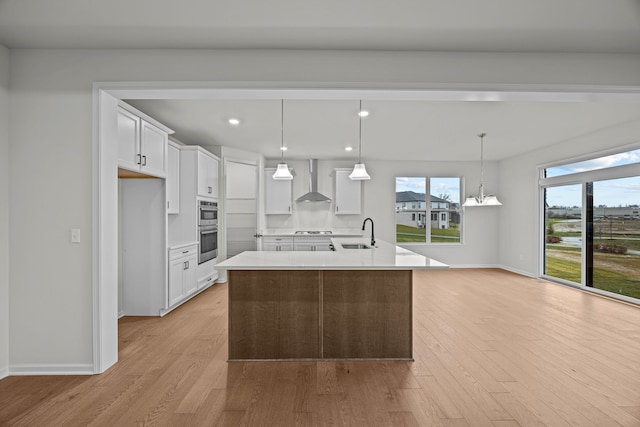 kitchen with light wood-style floors, light countertops, wall chimney range hood, white cabinetry, and a sink