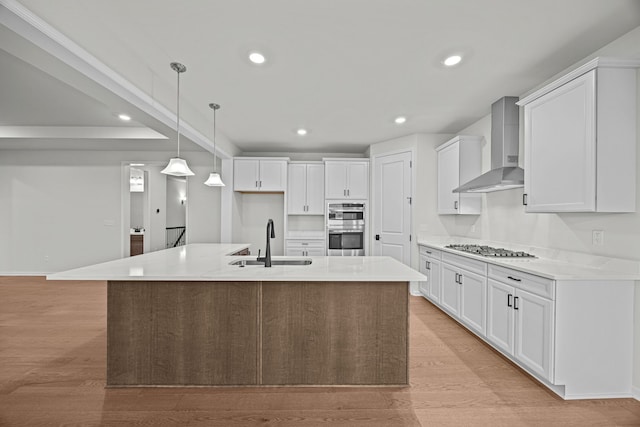 kitchen featuring recessed lighting, appliances with stainless steel finishes, a sink, light wood-type flooring, and wall chimney exhaust hood