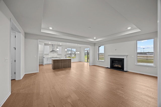 unfurnished living room with light wood-style floors, a tray ceiling, and a glass covered fireplace