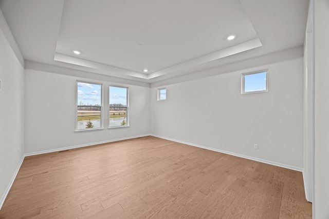 empty room featuring a tray ceiling, wood finished floors, and baseboards