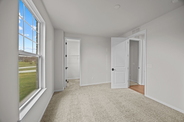 unfurnished bedroom with carpet floors, a spacious closet, visible vents, and baseboards