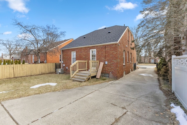 back of house featuring a shingled roof, fence, cooling unit, and brick siding