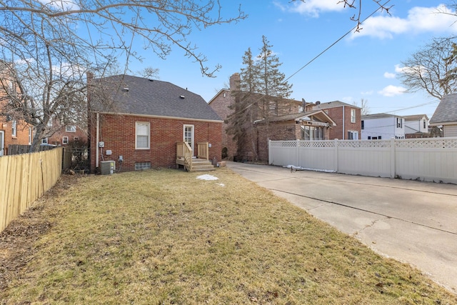 rear view of property featuring fence private yard, central AC unit, a lawn, and brick siding