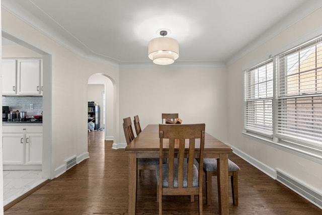 dining space featuring dark wood-style floors, visible vents, arched walkways, and crown molding