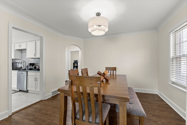 dining room featuring arched walkways, crown molding, visible vents, wood finished floors, and baseboards