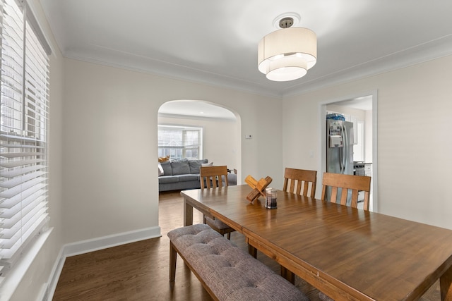 dining room with arched walkways, baseboards, wood finished floors, and crown molding