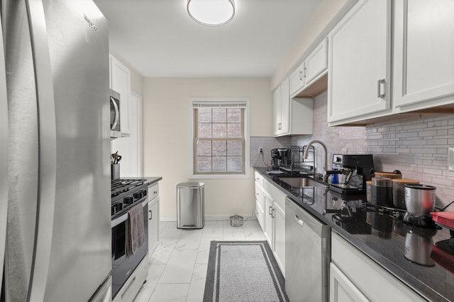 kitchen with marble finish floor, backsplash, appliances with stainless steel finishes, a sink, and baseboards