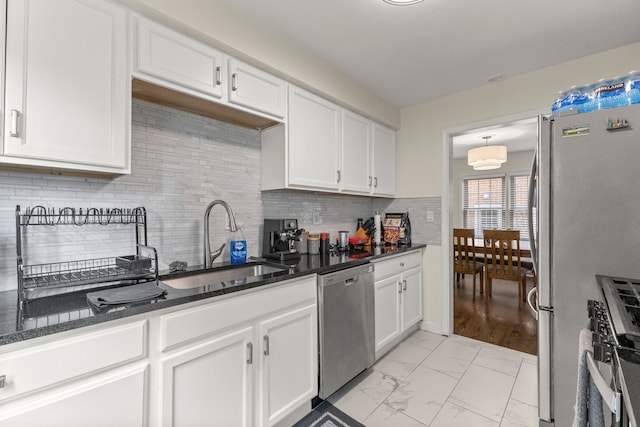 kitchen featuring dark stone counters, marble finish floor, stainless steel appliances, white cabinetry, and a sink