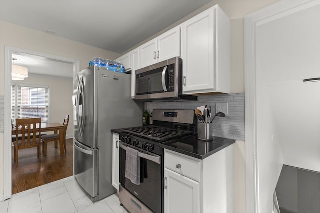 kitchen featuring stainless steel appliances, dark countertops, white cabinetry, and tasteful backsplash