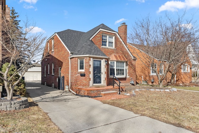 view of front facade featuring brick siding, a detached garage, a chimney, a shingled roof, and an outdoor structure