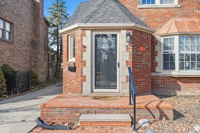 property entrance featuring a shingled roof, aphalt driveway, and brick siding