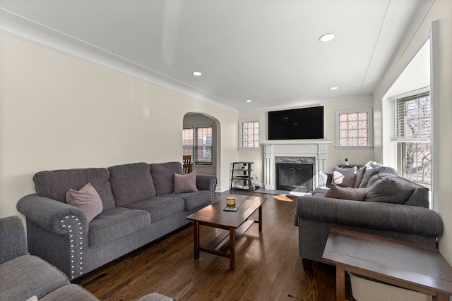 living area with arched walkways, a high end fireplace, ornamental molding, dark wood-type flooring, and recessed lighting