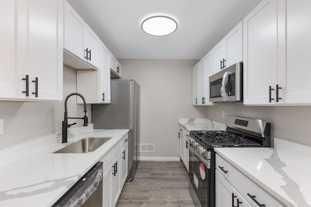 kitchen with stainless steel appliances, light stone counters, a sink, and white cabinets