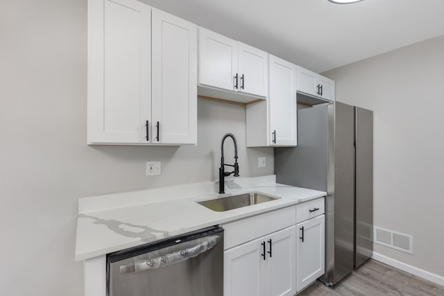 kitchen with light stone counters, stainless steel appliances, a sink, visible vents, and white cabinetry