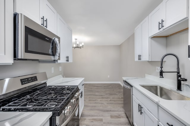 kitchen with a sink, baseboards, white cabinets, appliances with stainless steel finishes, and light wood-type flooring