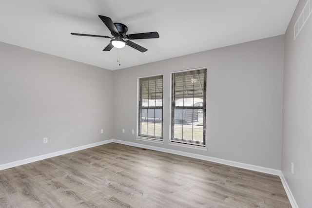 spare room with a ceiling fan, wood finished floors, visible vents, and baseboards