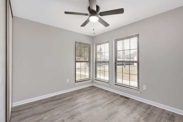 spare room with a ceiling fan, visible vents, baseboards, and wood finished floors