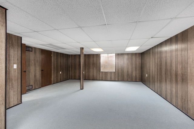 basement with a paneled ceiling, light colored carpet, and wooden walls