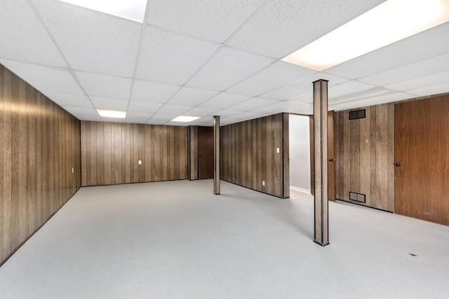 finished basement featuring a paneled ceiling, wooden walls, and visible vents