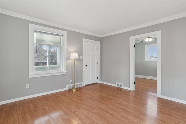 spare room with light wood finished floors, baseboards, visible vents, and ornamental molding