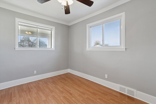 empty room featuring light wood finished floors, visible vents, a ceiling fan, ornamental molding, and baseboards