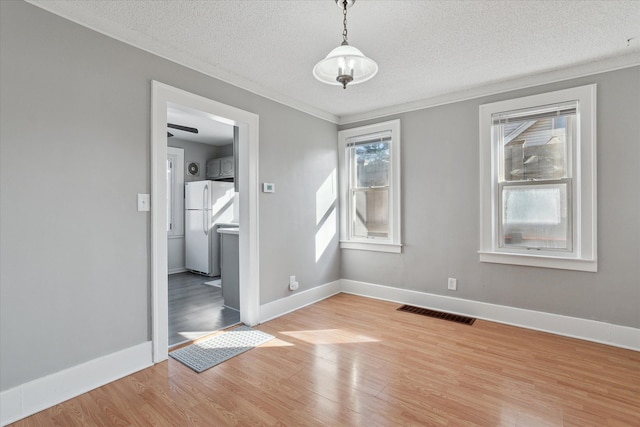 unfurnished dining area featuring a textured ceiling, light wood-type flooring, visible vents, and baseboards