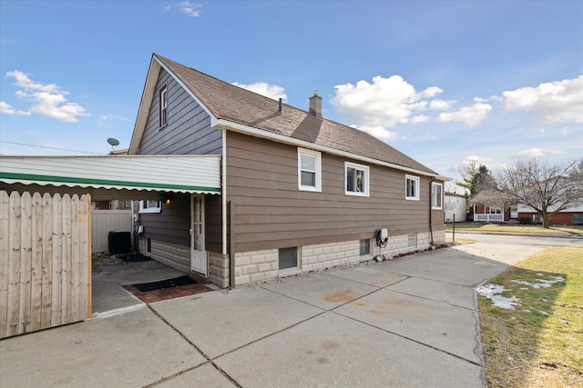 view of home's exterior featuring a shingled roof, fence, a chimney, and a patio