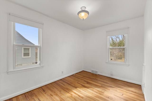 empty room with light wood-style floors, visible vents, and baseboards