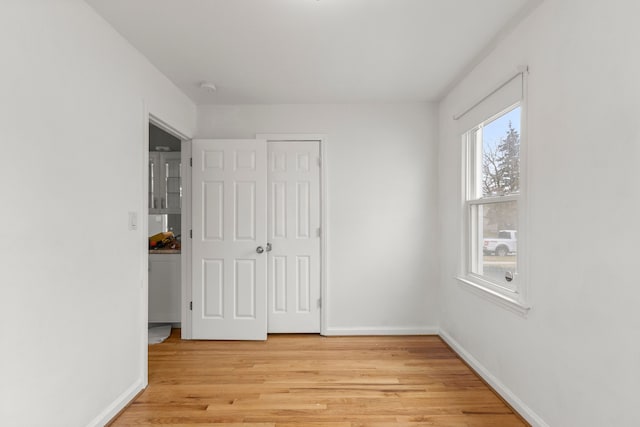 unfurnished bedroom featuring light wood-style floors, baseboards, and a closet