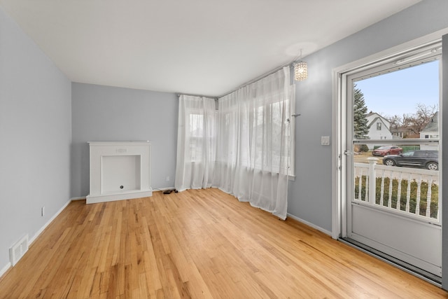 unfurnished living room featuring a notable chandelier, wood finished floors, visible vents, and baseboards