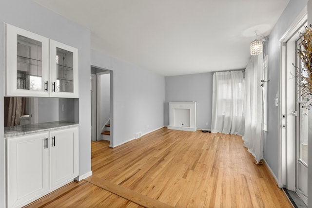 interior space with baseboards, visible vents, light wood-style flooring, stairway, and a notable chandelier