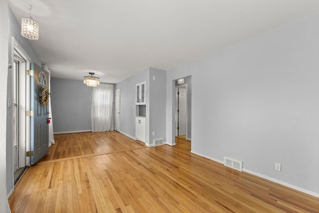 unfurnished room with visible vents, a notable chandelier, light wood-style flooring, and baseboards