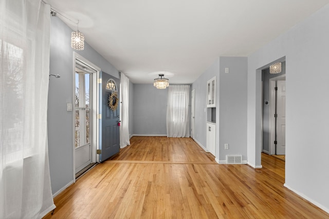 foyer entrance featuring baseboards, light wood finished floors, visible vents, and an inviting chandelier