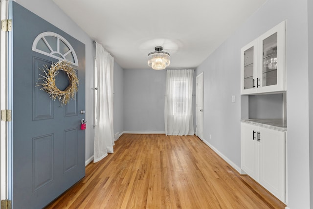 entryway featuring a chandelier, light wood-style flooring, and baseboards