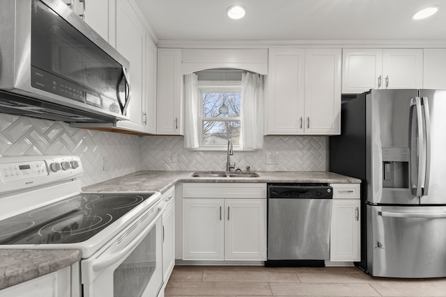 kitchen featuring stainless steel appliances, light countertops, backsplash, white cabinets, and a sink