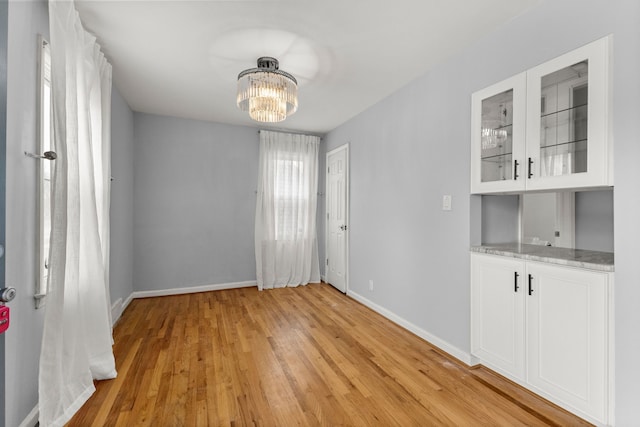 unfurnished room featuring light wood-style floors, a notable chandelier, and baseboards