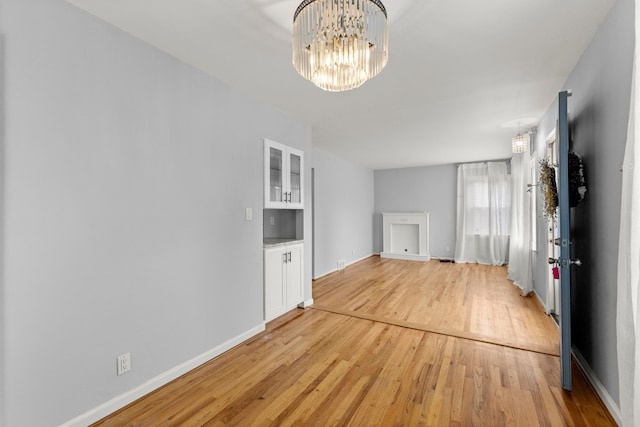 interior space featuring light wood-style floors, a notable chandelier, and baseboards