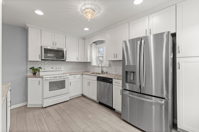 kitchen featuring a sink, white cabinetry, light wood-style floors, appliances with stainless steel finishes, and backsplash