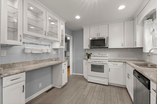 kitchen with light wood finished floors, stainless steel appliances, decorative backsplash, white cabinetry, and a sink