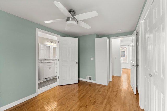 unfurnished bedroom featuring baseboards, visible vents, light wood-style flooring, ensuite bathroom, and a sink