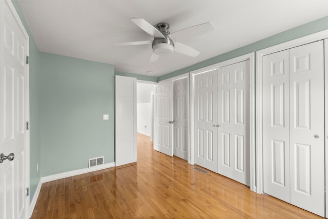 unfurnished bedroom featuring light wood-style floors, visible vents, baseboards, and two closets