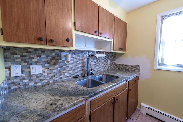 kitchen featuring brown cabinets, backsplash, a baseboard heating unit, light tile patterned flooring, and a sink