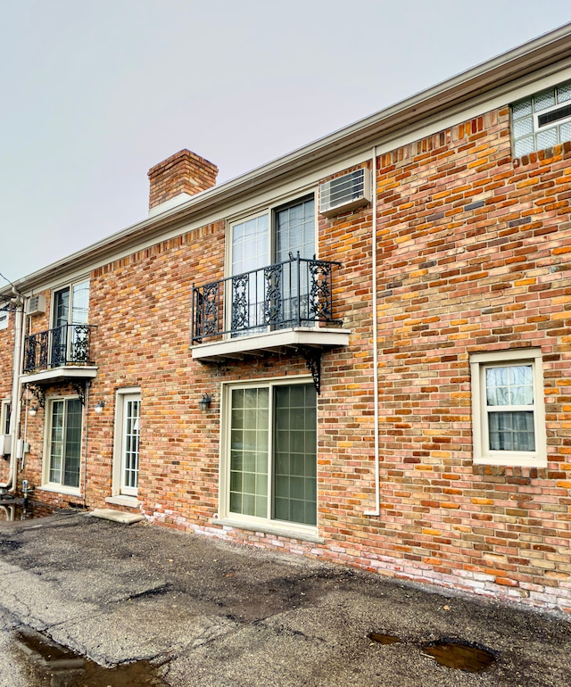 back of property featuring an AC wall unit, brick siding, a chimney, and a balcony