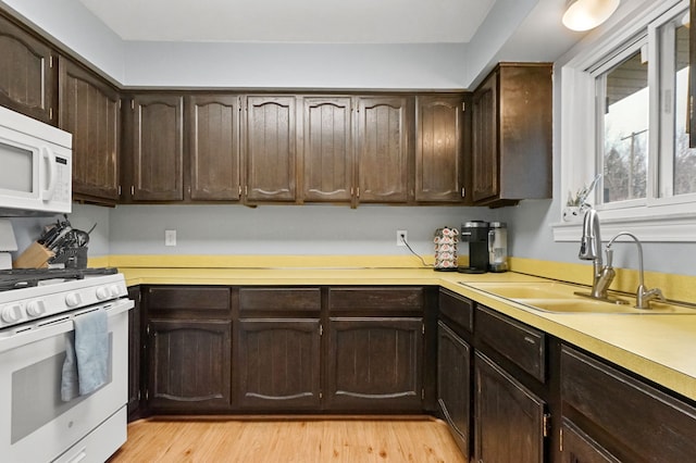 kitchen featuring light wood finished floors, light countertops, white appliances, and a sink