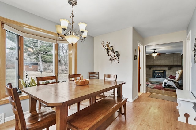 dining space featuring ceiling fan with notable chandelier, a fireplace, visible vents, baseboards, and light wood-type flooring