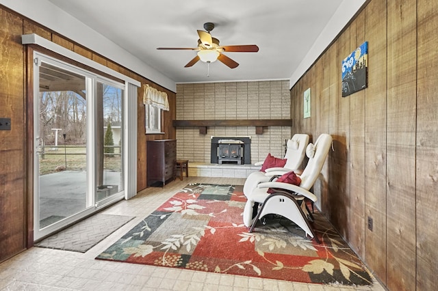 interior space featuring a healthy amount of sunlight, a wood stove, wooden walls, and a ceiling fan