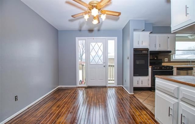 kitchen with baseboards, white cabinets, black range with gas cooktop, wood-type flooring, and a warming drawer